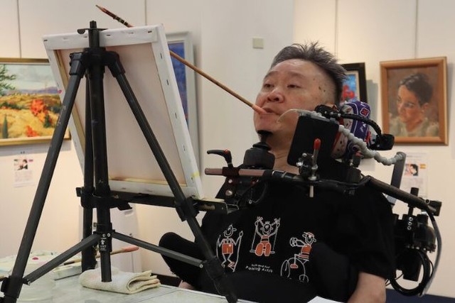 口で絵筆を使って描く画家の飯原孝さん（筆者撮影）